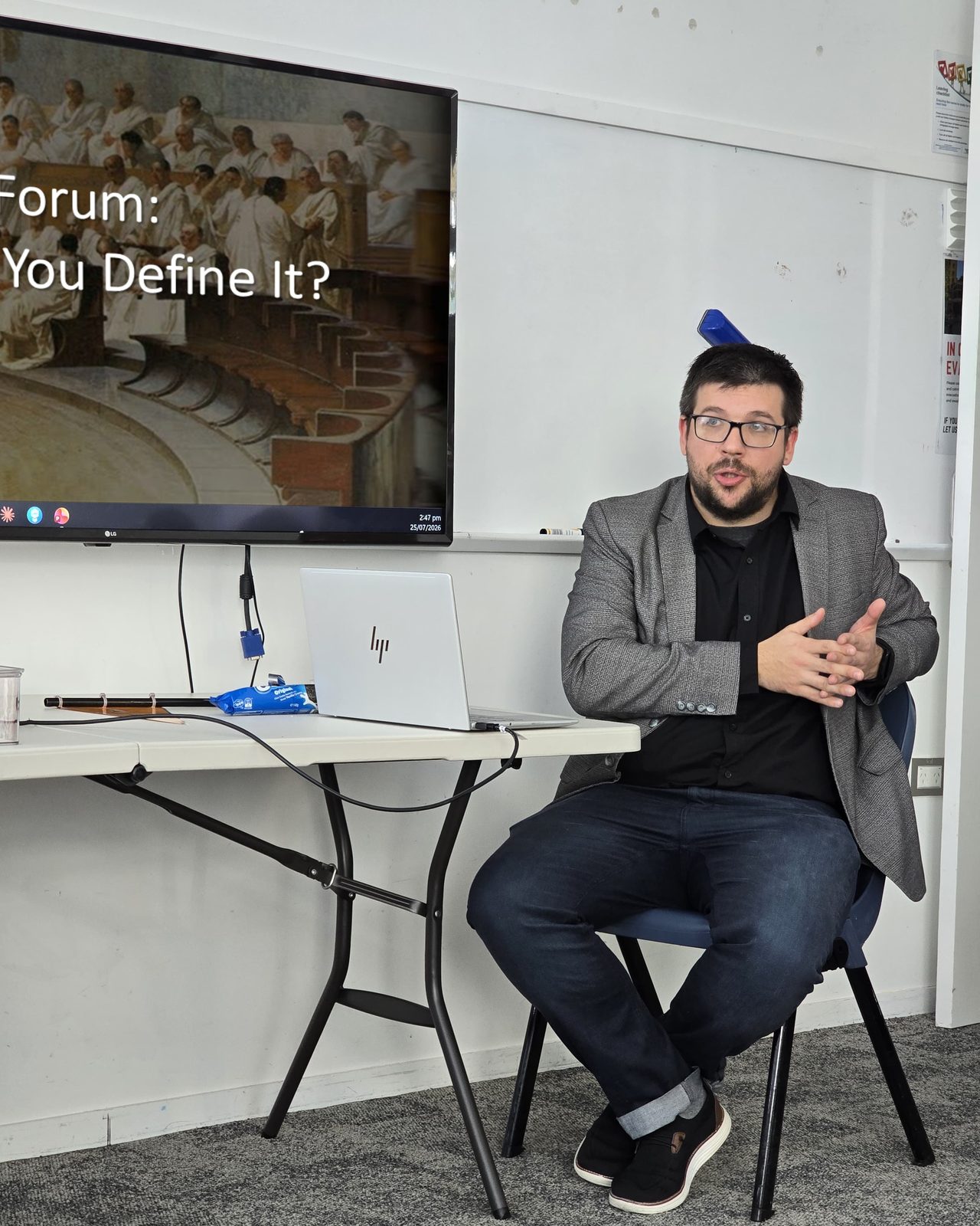 Dr Dmitry Zavialov facilitating The Civic Room public forum, seated in front of a screen reading Forum: You Define It