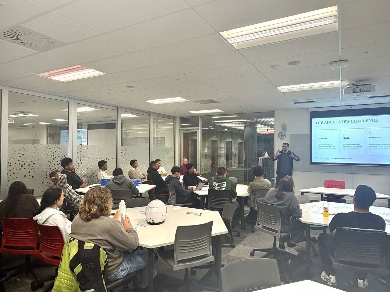 A full room of students at tables facing a screen headed The Advocate's Challenge, at the AUT Law Students' Society